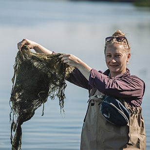 A photo of Mariena Hurley holding up plant growth from a river.
